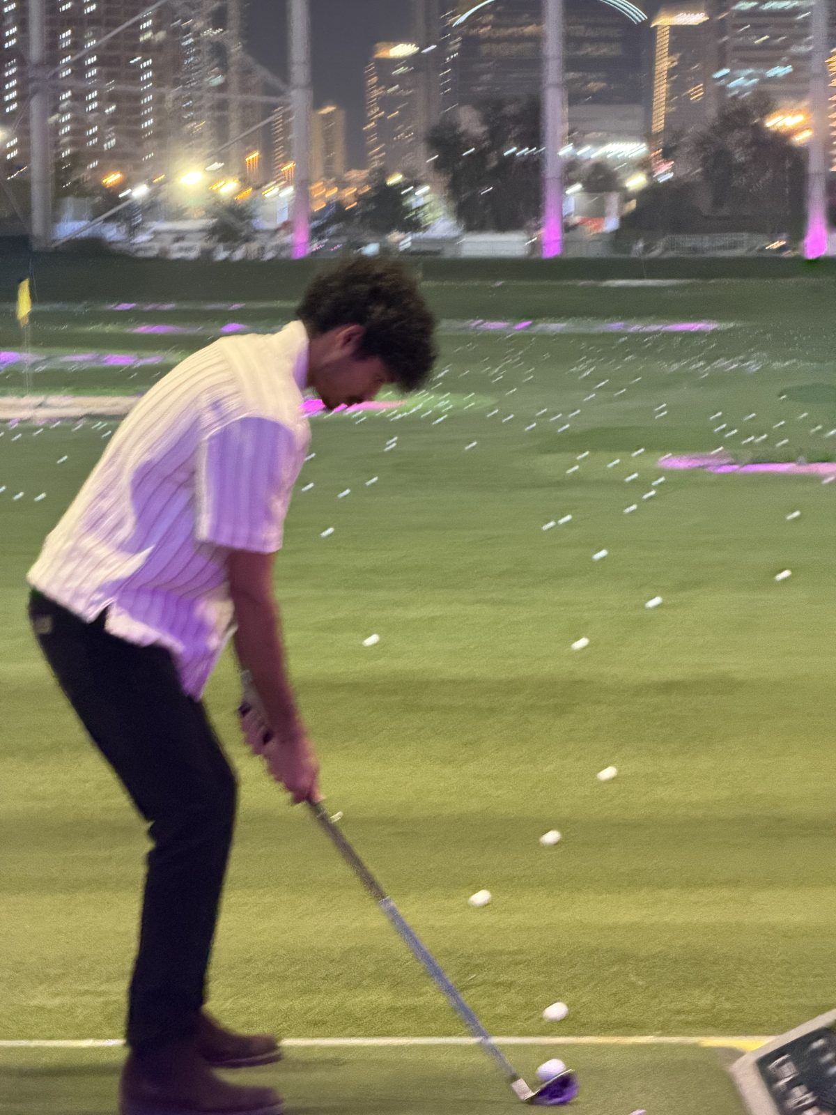 Aatmik Panse lining up a shot at a floodlit golf driving range at night