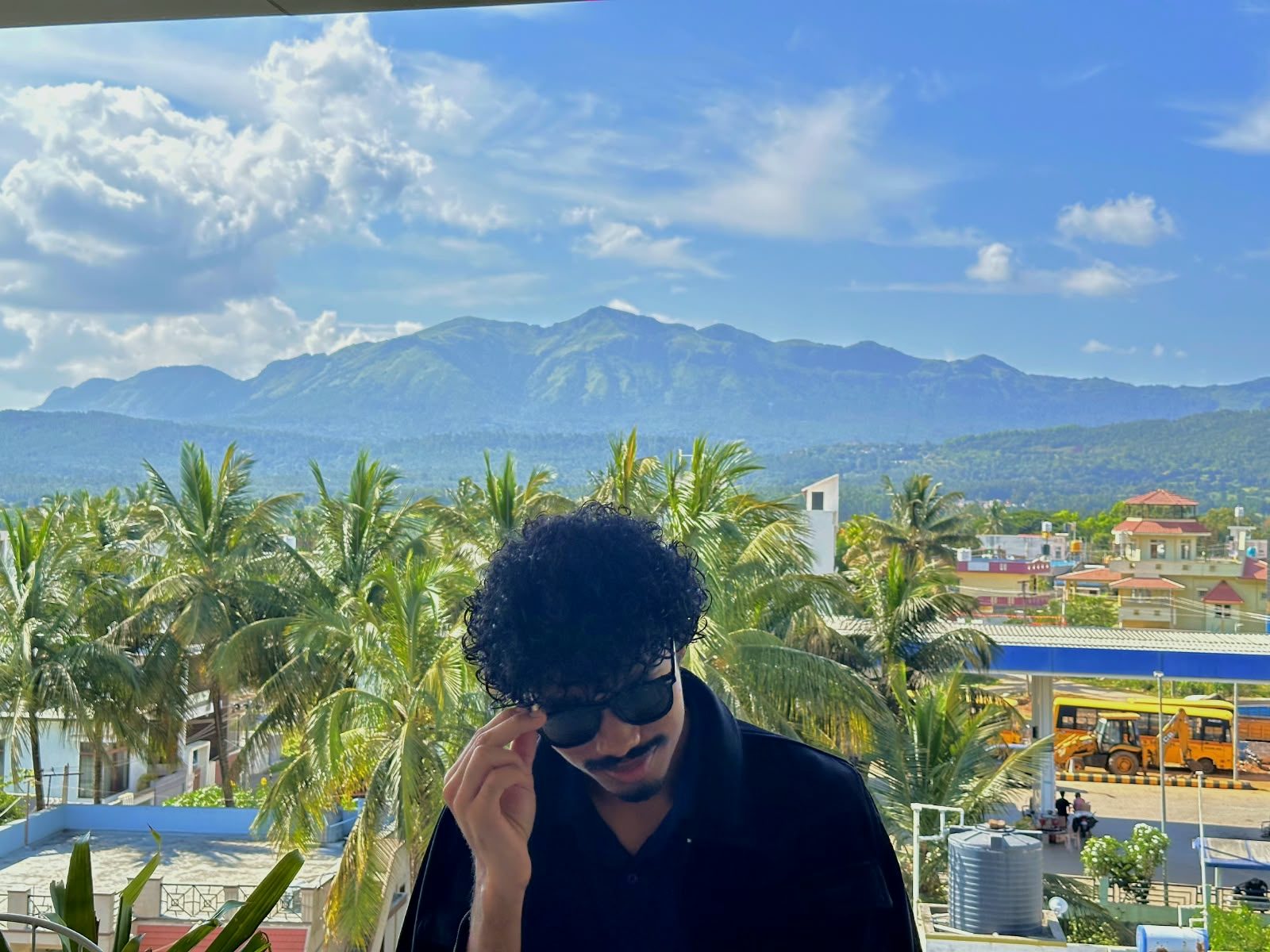 Aatmik Panse in sunglasses on a balcony, with green mountains and coconut palms behind him